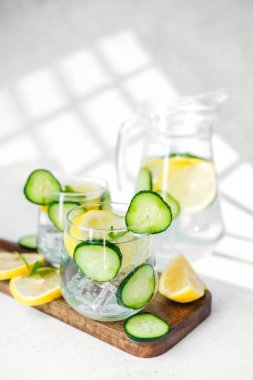 Salatalık limonlu su, tahta tahtada nane, beyaz masada güneş ışığı.