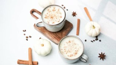 Mini balkabakları ve tarçın çubuklarının yanında tarçınlı iki fincan kremalı içecek.