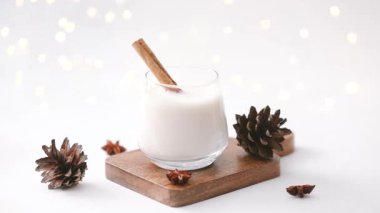 Tarçın çubuklu kremalı kış içeceği ve bulanık ışıklı tahta üzerinde çam kozalakları.