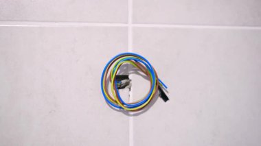 Sarmalanmış elektrik kabloları. Beyaz duvar inşaatında mavi sarı yeşil kahverengi.