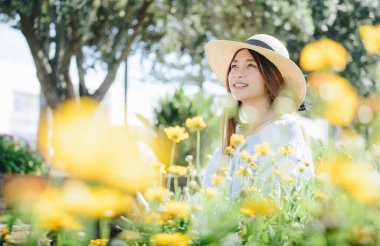 Bahçede oturan sarı çiçekli güzel Asyalı kadının portresi. Bahçede dinlenirken Asyalı genç bir kadının doğal güzelliği.