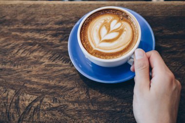 Cropped shot view of human hand with a cup of hot coffee latte.