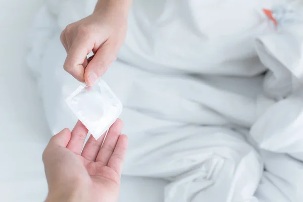 拍到的夫妇双手的镜头把避孕套给了床上的伴侣 拯救性爱 避孕套是避孕的 — 图库照片