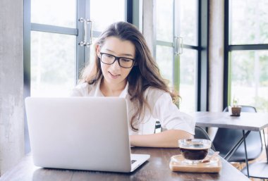 Genç melez iş kadınının portresi kahve molası verir ve modern ofisteki dizüstü bilgisayarında bir şeylere bakar. İş kadını yaşam tarzı kavramı.