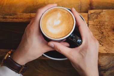 Birisi elinde sıcak bir fincan kapuçino kahveyi tutuyor. Cappuccino mükemmel bir espresso, buğulanmış süt ve köpük dengesidir..