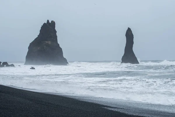 Stock image Reynisfjara or the Black Sand beach of southern Iceland with the iconic rock formation Reynisdrangar in dramatic mood and sky.