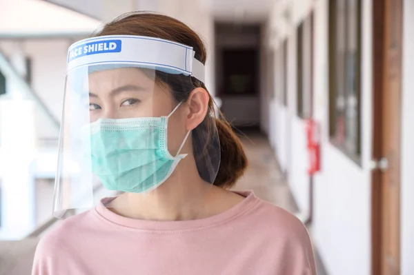 Asian woman wearing mask and face shield before going outside her room for prevent and protection covid-19 virus disease.