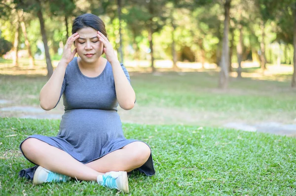 Pregnancy woman having headache and dizziness while her sitting in the park. Dizziness is one of the most common pregnancy symptoms, caused because your growing uterus puts pressure on blood vessels.