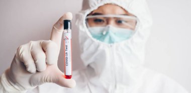 Hemşire / Doktor PPE giysisi giyiyor ve üzerinde 2019 nCoV analizi için kan olan bir test tüpü tutuyor. Solunum koronavirüsü hastalığı 2019 için laboratuvar testi kavramı.