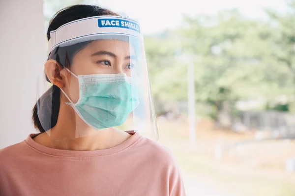 Asian woman wearing mask and face shield before going outside her room for prevent and protection covid-19 virus disease. Conceptual of new normal lifestyle after Covid-19 pandemic outbreak.
