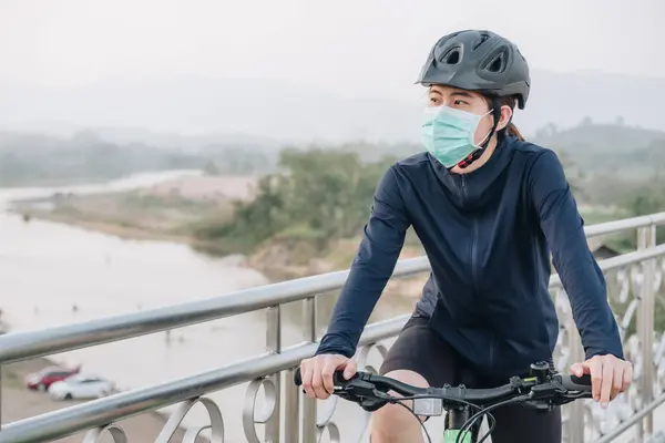 Portrait of young woman wearing a mask while riding a bicycle outdoor for protect and prevent the spread of virus. Conceptual of new normal lifestyle, everybody should wearing a mask when go outdoor.