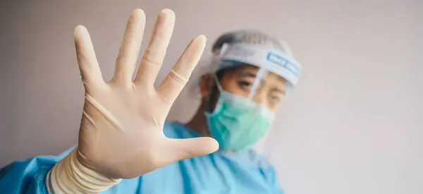 Doctor wearing PPE suit for protect virus and show stop hand gesture for social distancing. Social distancing is the physical space between people to avoid spreading illness.