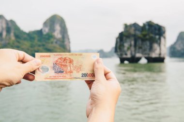 Vietnam 'daki UNESCO dünya mirası sahalarındaki Halong Körfezi' nde ikonik bir karst ile birlikte 200.000 dong Vietnam banknotlarını gösteren biri..