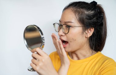Genç Asyalı kadın sivilce ve yara izlerine bakarken küçük bir ayna ile şok geçiriyor. Kadın yüzünde akne ve problem derisinin kavramsal görüntüsü.
