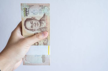 Beyaz arka planda izole edilmiş binlerce Tayland baht banknotunu tutan biri. Baht Tayland 'ın resmi para birimidir..