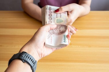 Birisinin diğerine bir tomar para (Tayland 1,000 Baht) verdiğini gösteren görüntüler. Tayland bahtı Tayland 'ın resmi para birimidir..