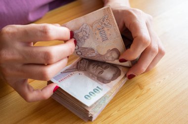 Tayland baht banknotlarını tutan ve sayan kırmızı tırnaklı bir muhasebeci kadın. Baht Tayland 'ın resmi para birimidir..