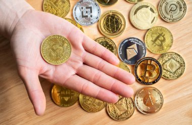 Arka planda çeşitli kripto para jetonları bulunan bir bitcoin jetonunu tutan kişinin yüksek açılı görüntüsü.