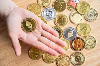 Arka planda çeşitli kripto para jetonları bulunan bir Ethereum jetonunu tutan kişinin yüksek açılı görüntüsü. Kripto para birimi, kriptografi ile korunan dijital veya sanal para birimidir..