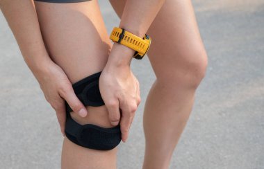 Diz ağrısından muzdarip olan kadının dizlerini tutarken çekilmiş görüntüsü ve dizinde ağrı olduğunda takılacak destek için dizlik takıyor..