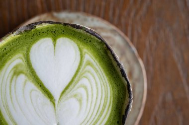 Ahşap masada servis edilen Matcha latte görüntüsü. Bir matcha latte kibrit tozu, su ve sütten oluşur.. 