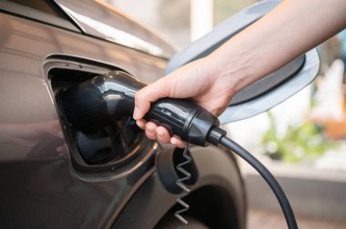EV araba sürücüsünün kırpılmış görüntü görüntüsü EV arabanın pillerini şarj etmek için elektrik konnektörünü yerleştirir.