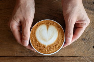 Kadın elleri içmeden önce bir fincan sıcak Cappuccino kahvesi tutuyor. Cappuccinoların tadı kremalı, pürüzsüz ve dengeli olarak tanımlanabilir..