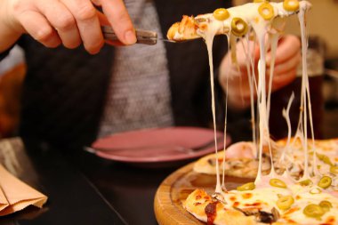 İtalyan pizzası dilimli, rendelenmiş Mozzarella 'lı Defocus kadın eli. Zeytinli pizza, fesleğen ve peynir yakın plan. Pizzacı dışarıda. Bulanık. Odaklanamıyorum.