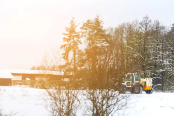 Defocus tractor clean snow sunny flare. Tractor cleaning snow in field. Big yellow tractor cleans up snow from the road and loads it into the truck. Out of focus.