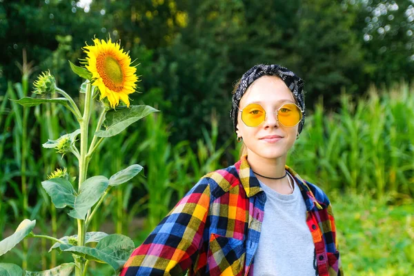 Defocus joyful teenage girl with sunflower enjoying nature on summer sunflower field. Portrait of adorable smiling girl in yellow sunglasses with sunflower on field, outdoors. Out of focus.