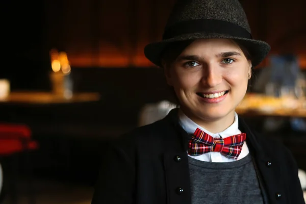 Woman wearing in british or english style clothes smiling indoor. Masculine woman. Young smiling woman wearing hat, bow tie and classic suit indoor. Happy freedom women. Nerdy person. Elegant style