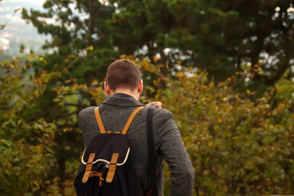 Back view of young brunette man walking. Man with rucksack in the forest. Back to school, Back of college student with backpack while going to university from park. Out of focus.