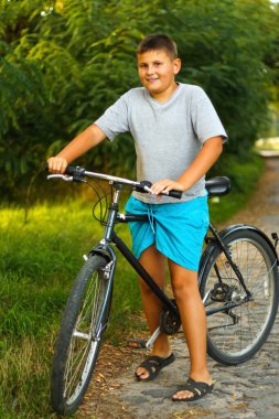 Mutlu çocuk yazın Park 'ta yarış pistine çıkar. Dışarıda bisikletle duran gülümseyen genç çocuk. Etkin yaşam.