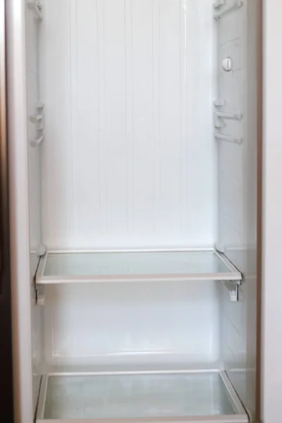 Empty open fridge with shelves, refrigerator. Inside of an empty white fridge. Vertical. Closeup. Out of focus.
