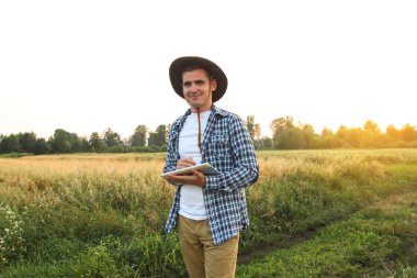 Çiftçi adam. Bir çiftçi, yemyeşil buğday tarlasının ortasında elinde bir tablet tutarak akıllı çiftlik kavramını somutlaştırıyor. Gün batımı.