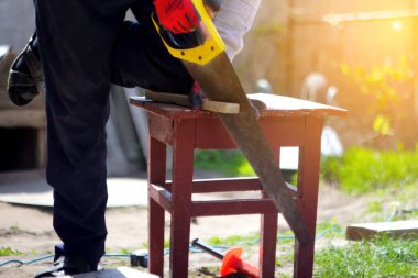 Bir şey kesmek için sarı testere kullanan bir adam var. Testerenin sapına odaklanırken, arka plan kasıtlı olarak bulanık. Odaklanamıyorum.