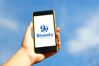 Bluesky uygulaması. Mavi gökyüzü arka planında sarı plastik çantalı akıllı telefon. Blue Sky yeni bir sosyal medya uygulaması ve metin paylaşım platformu. Volodymyr, Ukrayna, 23 Ekim 2022.
