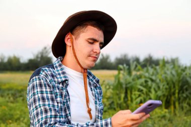 Çiftçi telefonu kullanıyor. Kendini işine adamış bir çiftçi dikilir, ekilen ekinleri dikkatle inceler..