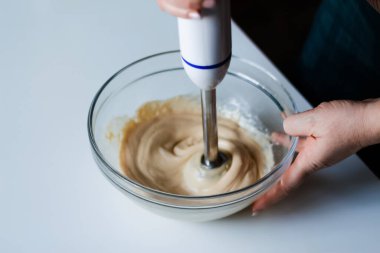 Bir şefin marifetli elleri ev yapımı mayonezle zeytinyağını karıştırıcı kullanarak harmanlıyor. Cam kasedeki kremalı sosun adım adım hazırlanışına dikkat edin. Odaklanamıyorum.