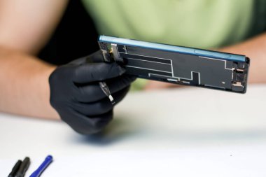 Telefonu tamir etmek için cımbız tutan bir erkek teknisyenin yakın çekimi. Eldiven takan ve elektronik cihazı tamir etmek için cımbız kullanan bir teknisyen. Acil durum telefonu. Kapat..