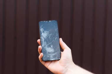 Kahverengi arka planda kırık cam ekran akıllı telefon. Mobil aygıtların onarımı ve kırılganlığı için ihtiyaç.
