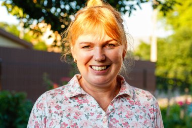 Gülümseyen olgun bir kadının portresi. Yaz yeşili doğa geçmişi. Yaz parkında orta yaşlı, sarışın bir kadının portresi. 40 'lı yaşlarda gülümseyen bir kadın..