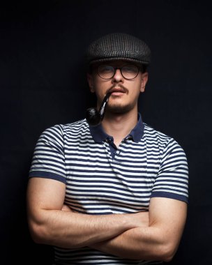 Şapkalı ve çapraz kollu bir denizciyle erkeklik kavramı. Beşik şapkalı ve kaslı kollu bir denizcinin yakın plan portresi. Siyah arkaplan.