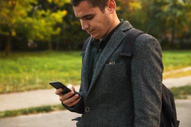 Yazın açık havada telefon kullanan genç bir işadamı, teknoloji ve doğa. Yazın açık havada akıllı telefon kullanan iş elbiseli bir adam..