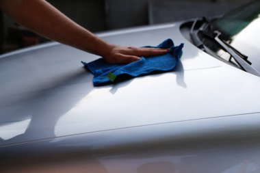 Arabanın kaputunu mavi bir bezle yıkayan bir adam. Araba bakımı: kaputu paçavrayla temizleyen adam. Otomotiv ve bakım işleri için uygun. Odaklanamıyorum. Bulanık.