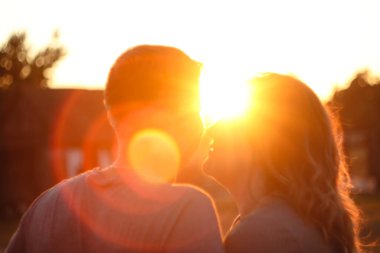 Canlı bir güneşin batışına ya da arka planda yükselişine karşı çiftlerin iç açıcı bir görüntüsü. Sahne aşk, umut ve mutluluk temalarını taşır. Bulanık, bulanık.