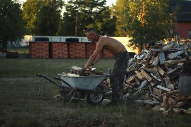 Bir adam yakacak odunla dolu bir el arabasıyla çalışırken, büyük bir yığın oluştururken ve istiflerken görülüyor. Odun yığınını düzenler..