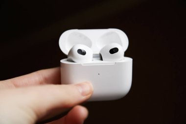 Pürüzsüz beyaz bir çantada kablosuz kulaklıkları tutan bir elin yakın plan görüntüsü..