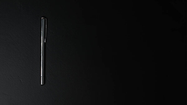 A silver pen with a sleek silver accent placed on a dark black background, creating a minimalist yet professional vibe. Banner for design with copy space.
