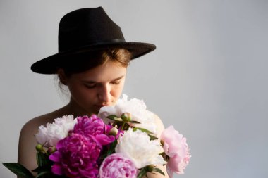 Canlı şakayık çiçekleriyle çevrili şık bir şapka takan güzel bir genç kadın. Bayrak, güzellik, moda veya çiçek kavramları için mükemmeldir. Kadınlık, gençlik ve çekicilik duygusunu yansıtır..